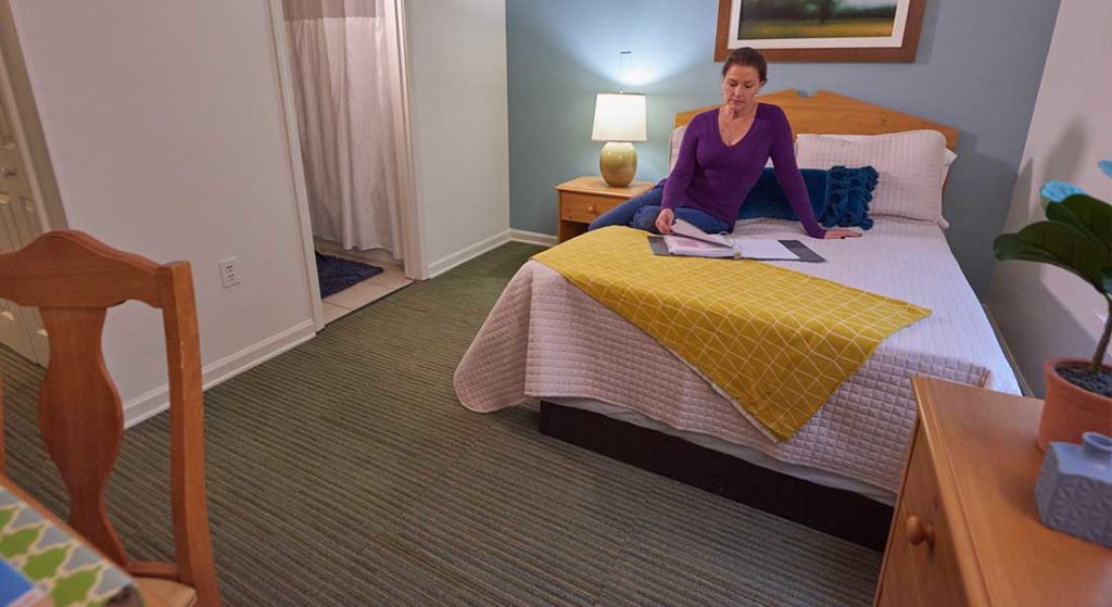 woman sitting on bed reading in residential treatment patient room at Skyland Trail South