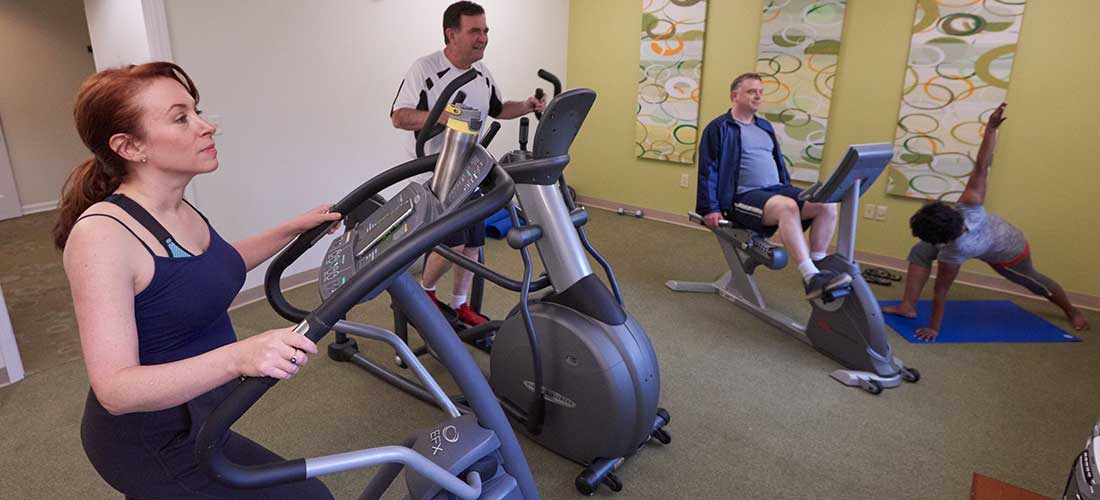 four adults on exercise equipment in a fitness room