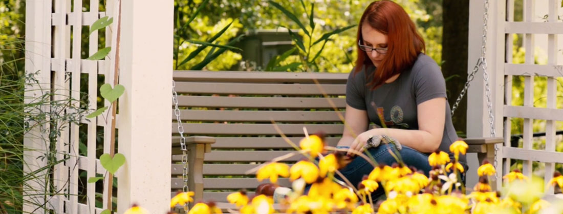 young woman writing in journal on wooden swing with flowers