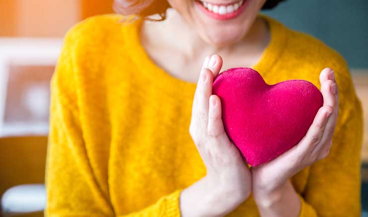 woman in a yellow sweater holding a red plush heart