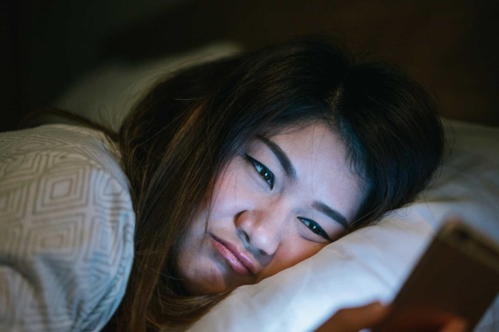 woman looking a smart phone in bed at night