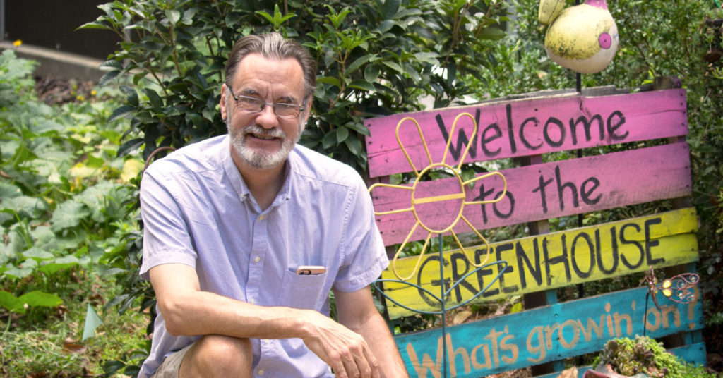 Man kneels next to greenhouse sign