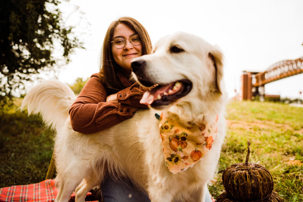 Alex B Growing Through Grace: Young woman with glasses and her golden retriever sitting on a picnic blanket in autumn.