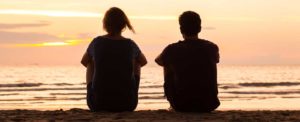 mom and adult son sitting together on beach in silhouette