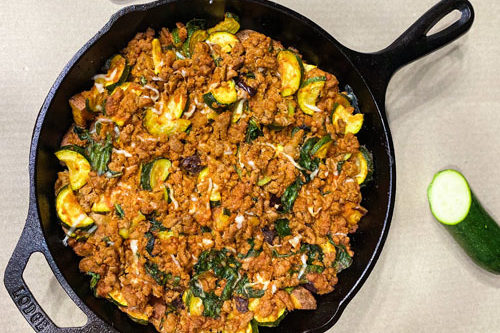 An overhead photo of the finished ground turkey skillet cooling in the cast iron pan alongside a slide of zucchini.