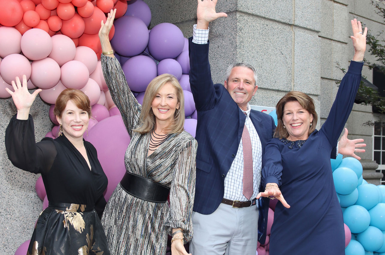 four people with arms out celebrating in front of colorful ballon display