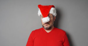 A man in a red shirt wearing a red santa hat that is covering his face