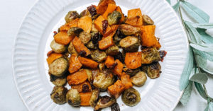 a top-down photo of roasted brussel sprouts and squash on a white plate