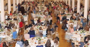 An overhead view of the Associates Luncheon: a large banquet room filled with circular tables and attendees listening to a speaker's presentation