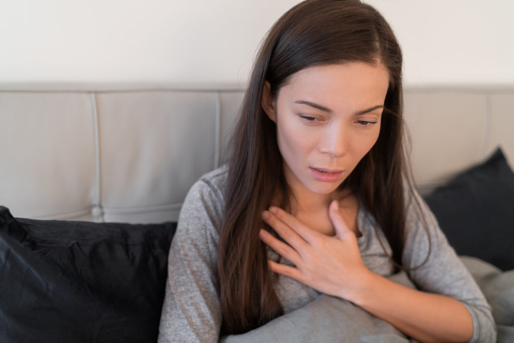 woman sitting in bed with hand over heart looking distressed