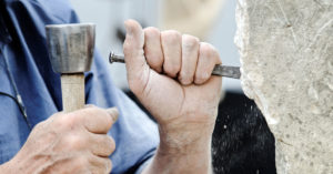 an image of hands holding a pick and hammer tools used to etch stone