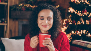 a grinning woman takes a deep breath above a mug during the holiday season