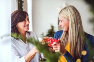 mother giving gift to adult daughter with evergreen in the foreground