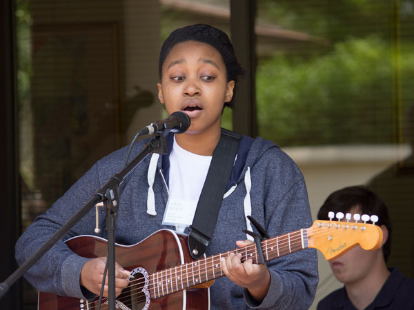 a woman strums a guitar while singing into a microphone at a previous Arts in the Garden