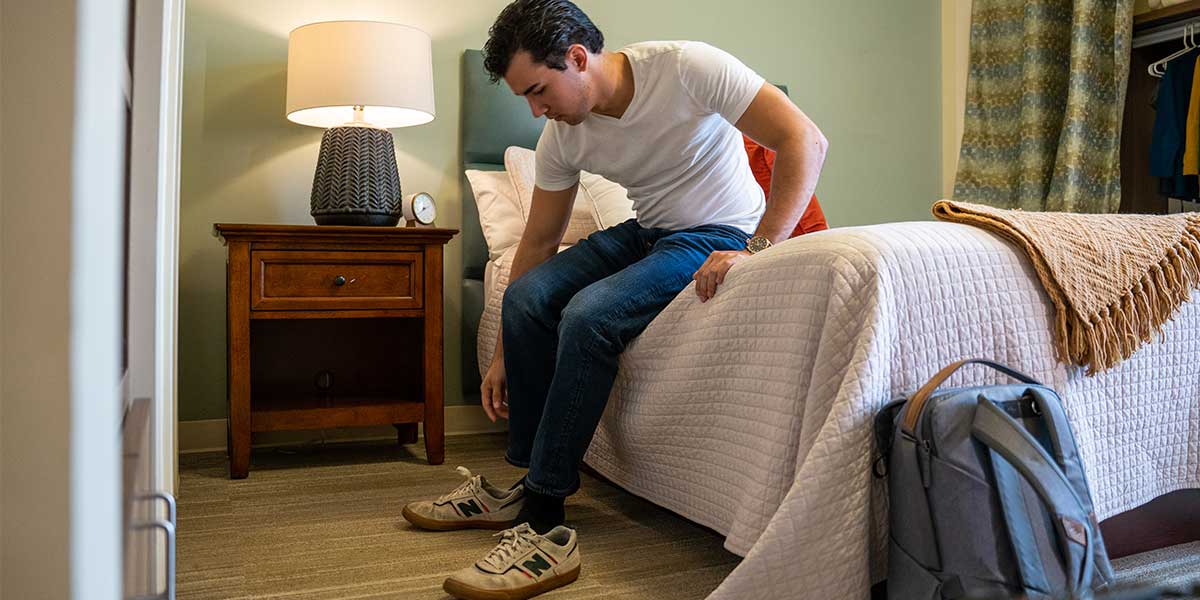 young man sitting on bed in bedroom putting on shoes