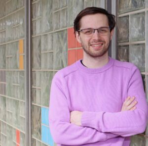 smiling young man in lilac sweater leaning against glass brick wall