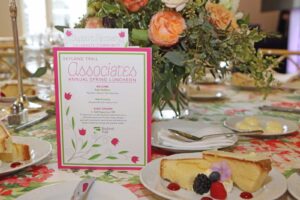 Event program with pink floral design sits on luncheon table next to flowers and dessert