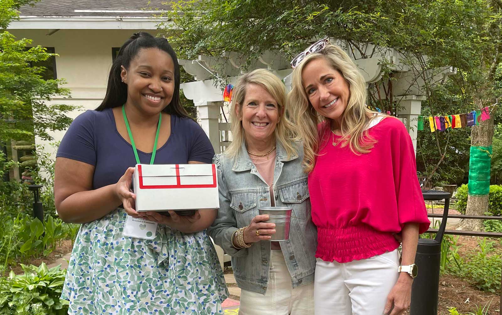 three women standing and smiling outdoors at arts in the garden event