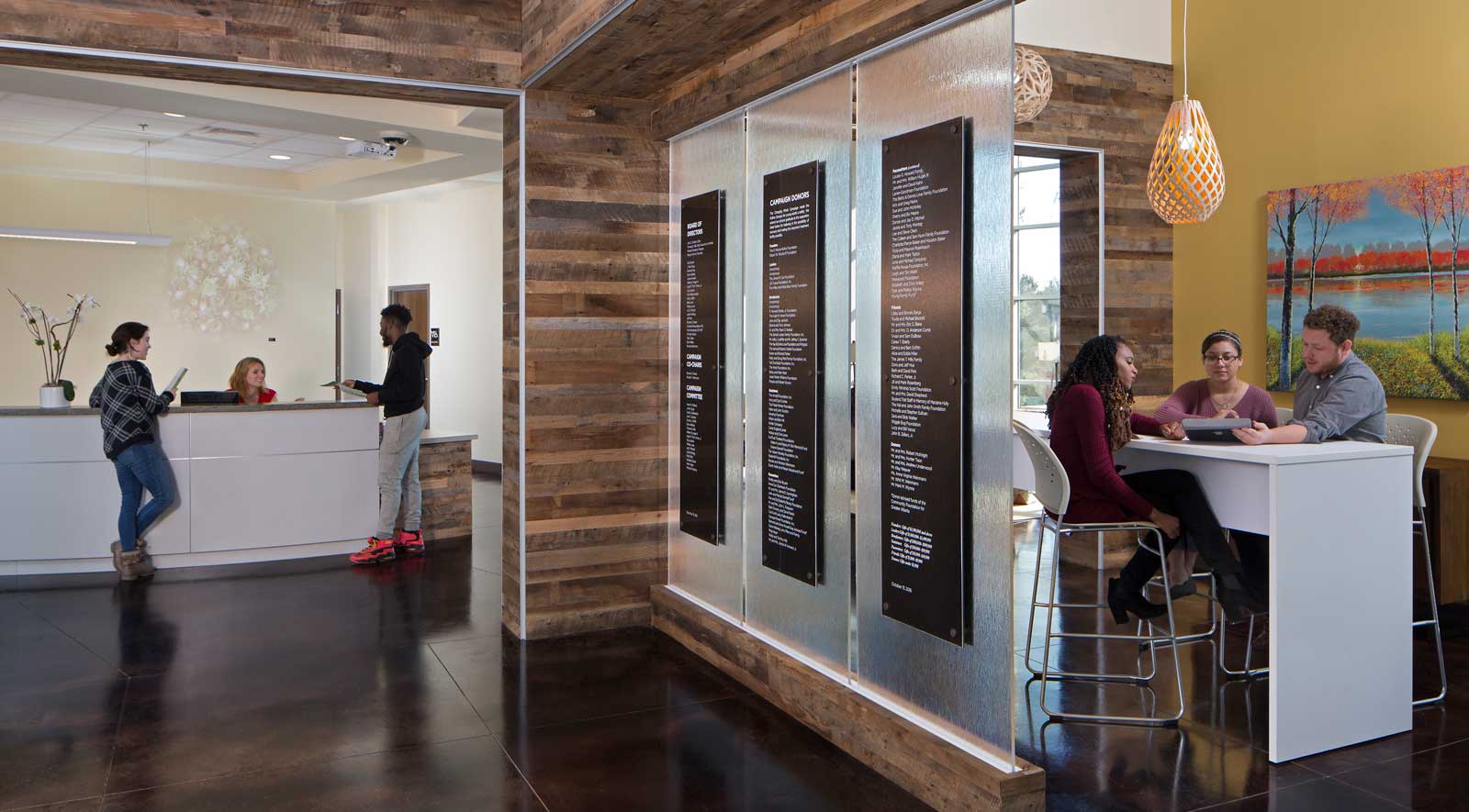 reception area and lobby of mental health treatment facility - two young adults stand talking to staff at reception desk and three adults sit at counter height table looking at laptop