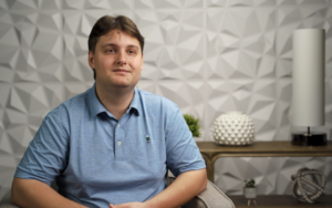 young mail in blue collared shirt seat in front of white backdrop