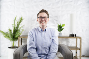 Young woman in blue oxford shirt, with glasses and short hair, seated