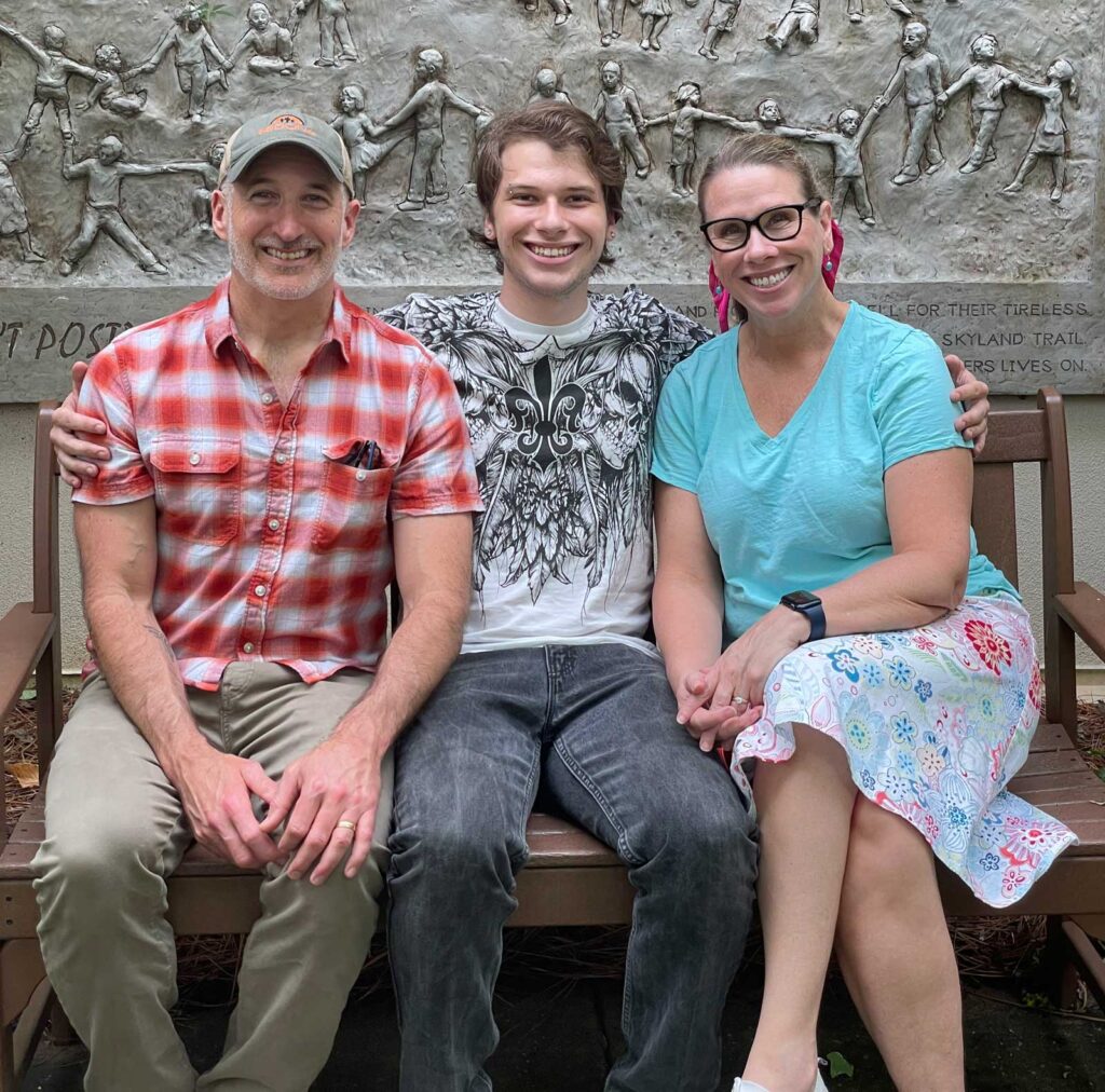 three people sitting on bench, father, adult son, mother, son with arms around mom and dad