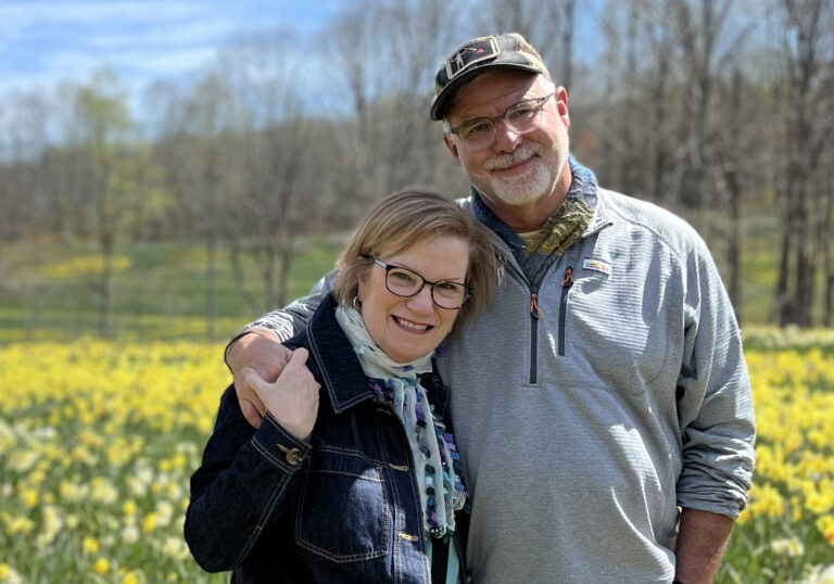 Woman and Man couple smiling and standing in front of field of yellow flowers