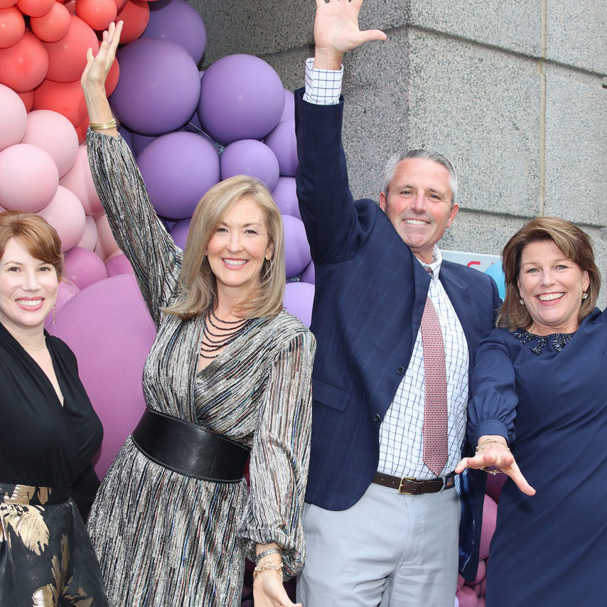 four people with arms out celebrating in front of colorful ballon display