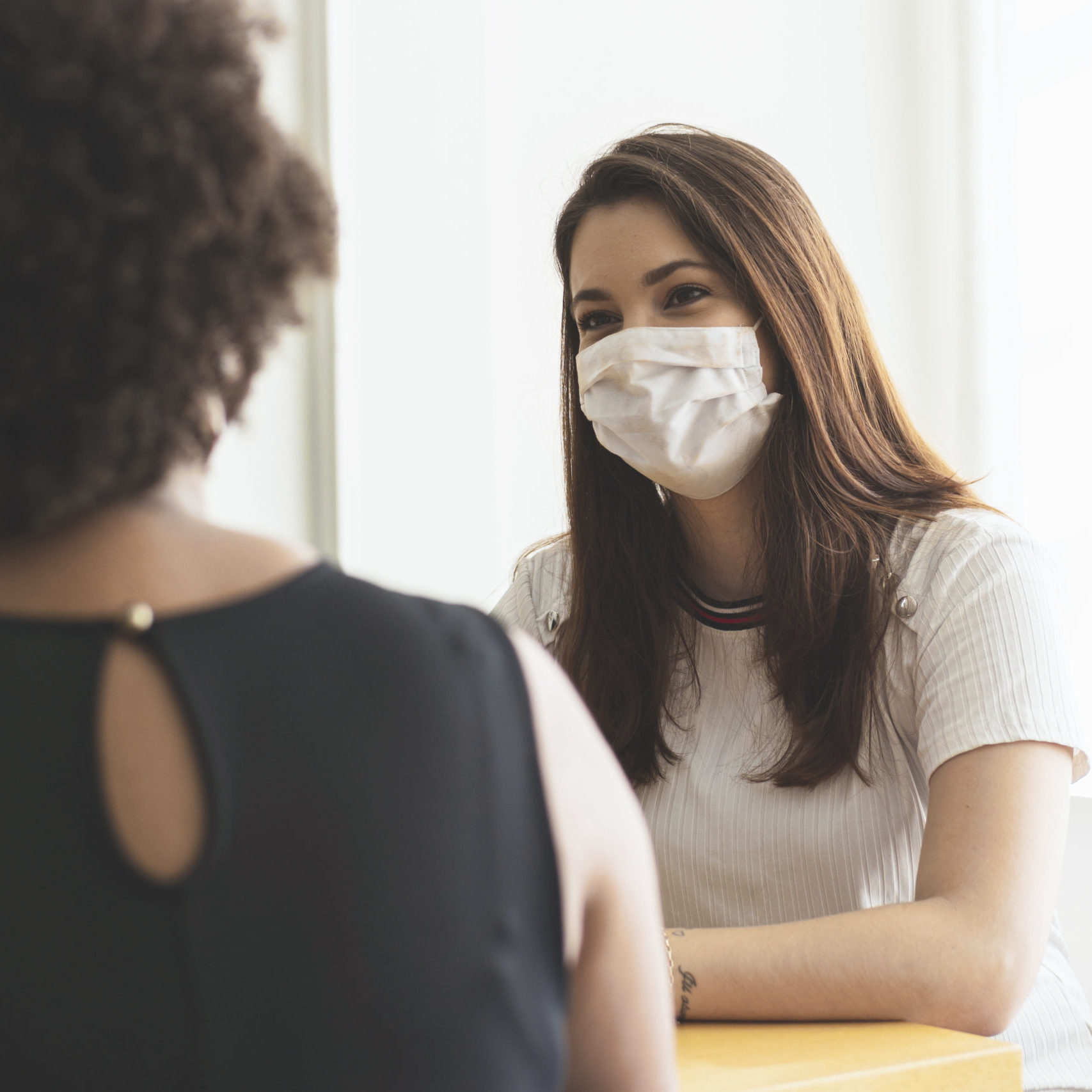 Two young women talking in an office wearing a protective face mask.